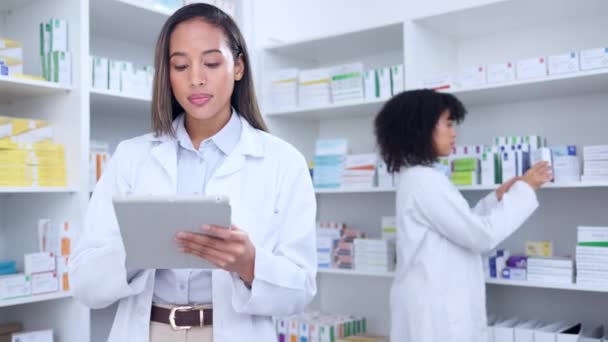 Pharmacist with digital tablet while doing stock update and counting inventory with a colleague in a pharmacy. Female chemist typing on device and searching pharma app or checking online prescription. - Video