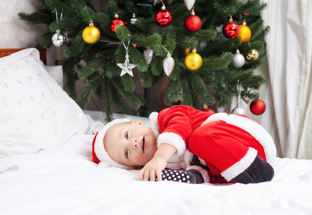 Baby boy in Santa costume lying on bed - 写真・画像