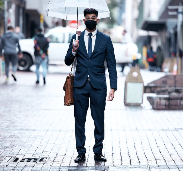 Its a startling new world were adapting to. Portrait of a young businessman wearing a face mask and holding an umbrella on a rainy day in the city - Foto, Imagen