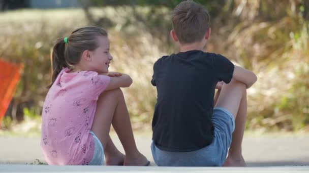 Dva šťastně se usmívající dospívající děti, chlapec a dívka sedí venku odpočívají a baví se v létě slunečný den. - Záběry, video