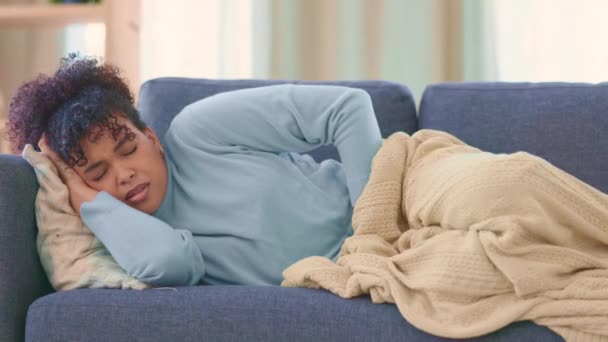 Woman suffering from PMS pain while laying on a sofa at home. Young female with chronic endometriosis covering herself with a blanket on a couch. Lady feeling unwell, in early stages of a miscarriage. - Video