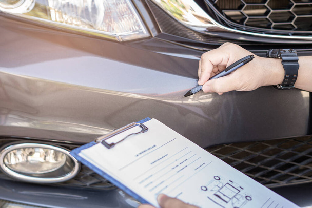 Close-up hand een man mark positie punt van auto-ongeluk op de voorbumper en schrijf detail op document om schade te eisen van de verzekering: auto verzekering concept - Foto, afbeelding