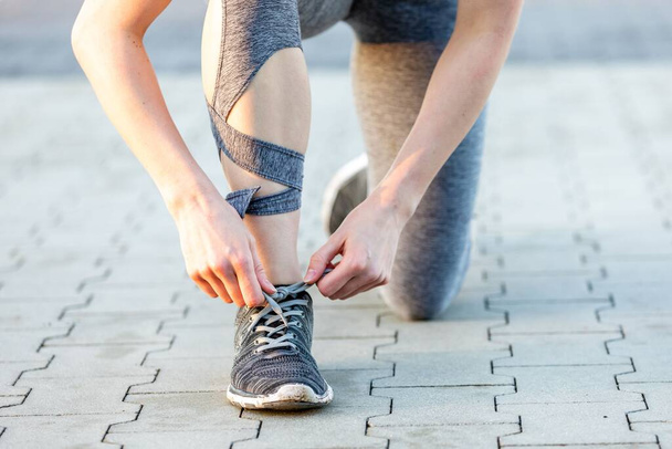 A closeup shot of a female runner ties shoelaces in the park - Foto, immagini
