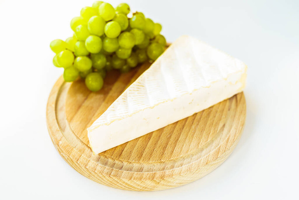 piece of brie cheese, white grapes on wooden round cutting board. Side view, close-up - Foto, Bild