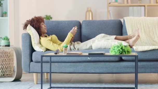 Relaxed black woman reading a funny book on a sofa at home. Young female spending free time with an interesting novel in a living room, enjoying the weekend by catching up with her favorite hobby. - 映像、動画