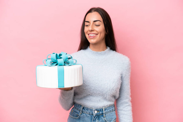 Young caucasian woman holding birthday cake isolated on pink background looking to the side and smiling - Foto, imagen