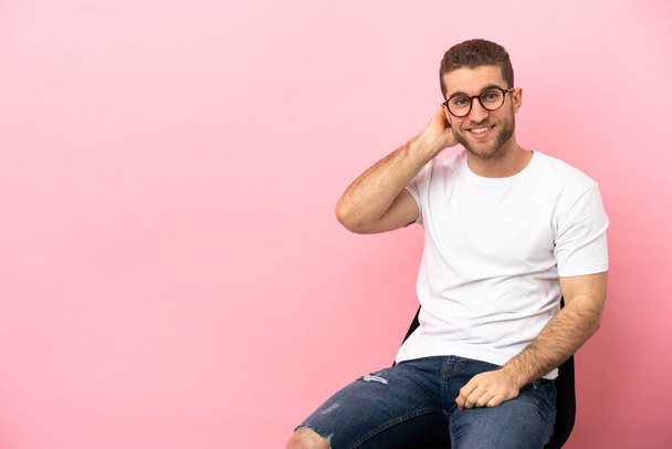 Young man sitting on a chair over isolated pink background laughing - Photo, Image