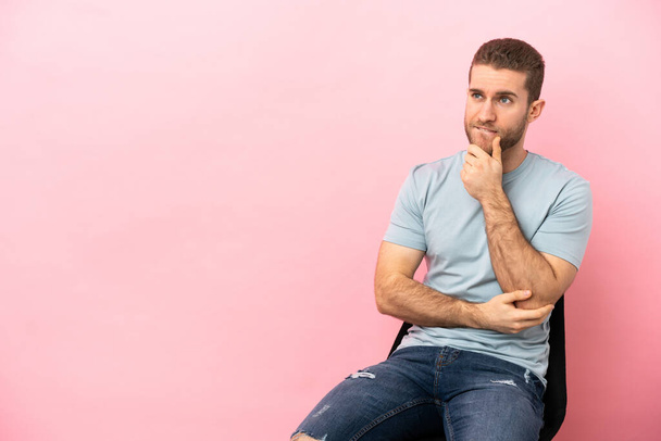 Young man sitting on a chair over isolated pink background having doubts and thinking - Photo, Image