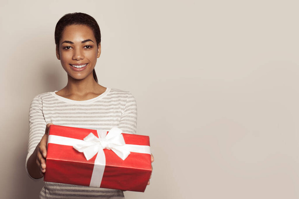 Retrato de una mujer negra feliz sonriendo y sosteniendo una caja de regalo roja - Foto, imagen