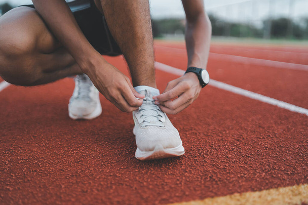 Runner man kneeling and tying shoelace on the lane at stadium, athlete sportman prepare to training for competition race. Sport running concept. - Fotografie, Obrázek