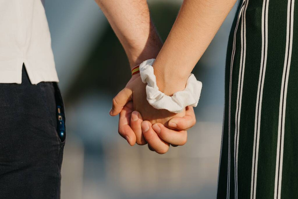 A close photo of hands which are holding each other in the modern urban space at the sunset in a Spain town. A couple of tourists on a date in the evening in Valencia. - 写真・画像