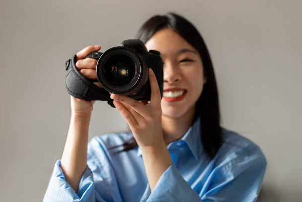 Fényképész karrier. Happy Asian Woman holding Camera Mosolyogva a kamerába Fényképezés Álló beltérben. Női fotós pózol fotókamerával. Kreatív hobbi koncepció - Fotó, kép