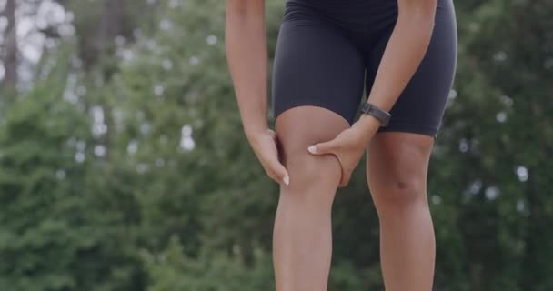 Спортсменка масажує коліно від болю, натираючи ногу, щоб вилікувати біль у парку з копіспазмом. Вмістити спортивну жінку, яка страждає від травми під час фізичних вправ в саду або лісі
. - Кадри, відео