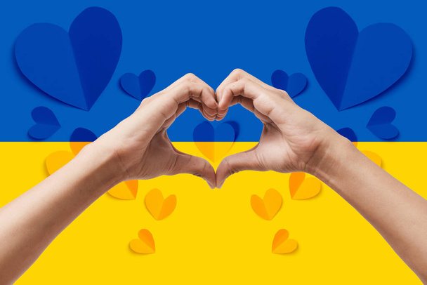 Man handen maken een hart vorm op Oekraïne vlag kleur achtergrond. Blijf bij het ukraine symbool. Hand hart liefde gebaar met Oekraïense vlag achtergrond. - Foto, afbeelding