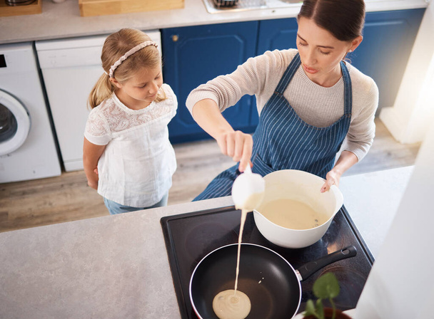 Show me how to make a good pancake, mom. a little girl watching her mother make pancakes - Фото, изображение