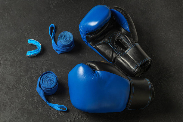 Blaue Boxhandschuhe mit Mütze und Bandagen auf schwarzem Hintergrund. - Foto, Bild