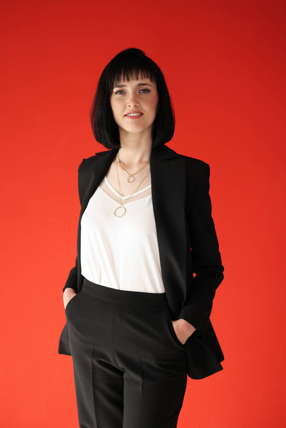 Beautiful female brunette business woman CEO in a black suit, isolated on red background, standing confidently with arms in pockets. Females in Business - Valokuva, kuva