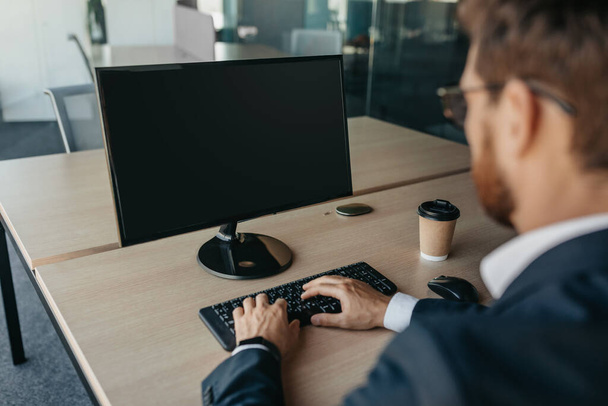Unrecognizable businessman using computer with empty screen at office, sitting at workplace, offering space for mockup on monitor. Male CEO showing place for online ad - 写真・画像