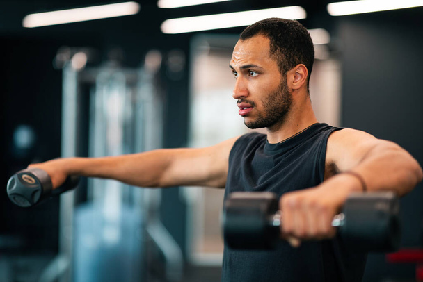 Portrét motivovaný africký americký mužský atlet trénink s činkami v tělocvičně, mladý černý sportovec cvičení v moderním fitness klubu interiér, cvičení svalové síly, kopírovat prostor - Fotografie, Obrázek