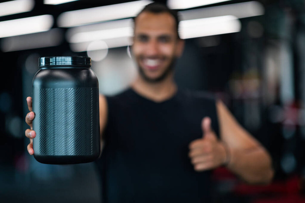 Fitness Nutrition. Happy Black Sportsman Holding Container With Whey Protein Powder And Gesturing Thumb Up At Camera, Smiling African American Male Athlete Recommending New Sport Nutrition Product - Foto, imagen
