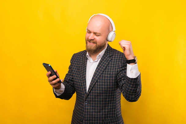 A photo of a young businessman listening to music and looking in his phone cheerfuly - Fotó, kép