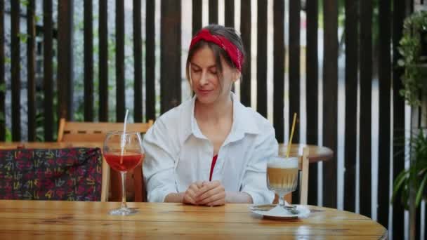 Счастливая девушка в кафе выбирает, что пить, кофе или коктейль. летний образ жизни и развлечения - Кадры, видео