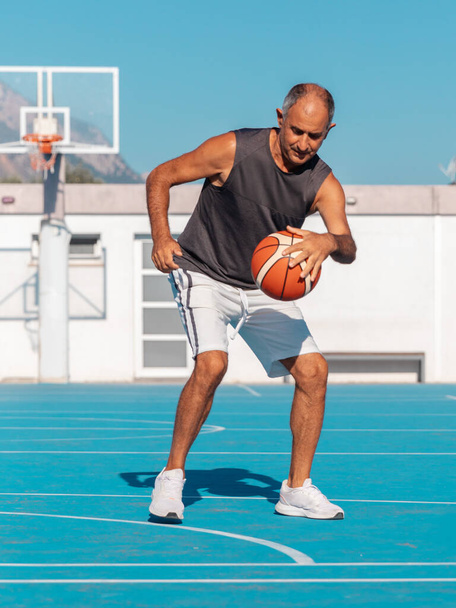 Adult senior man playing a sport ball on blue basketball court at summer sunny day - Zdjęcie, obraz