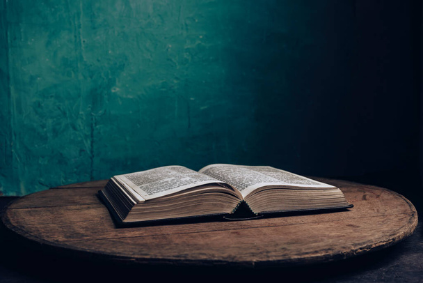 Belle Bible ouverte sur une vieille table en bois de chêne brun. Fond de mur vert. - Photo, image