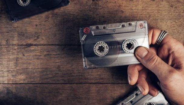 Hand vasthouden audio cassette tape op bruine oude houten tafel. Minimalisme retro stijl concept. Achtergrondpatroon voor ontwerp.  - Foto, afbeelding