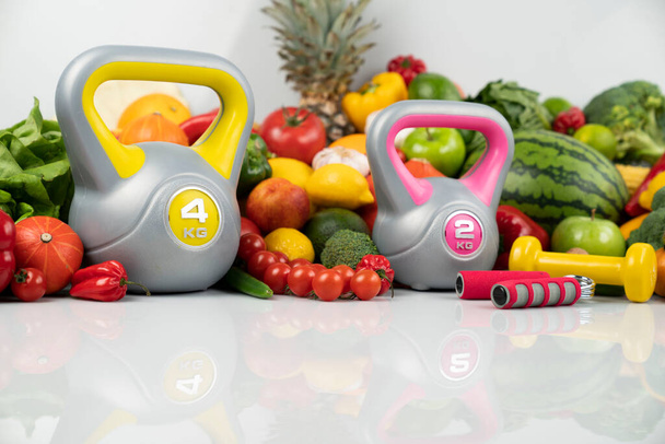 Fitness concept. Healthy nutrition: fruits and vegetables. Equipment for fitness exercises: weighing machine and dumbells. White background. - Photo, Image