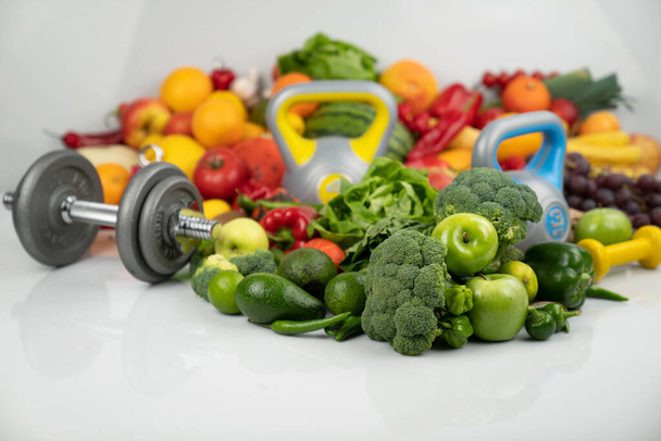 Fitness concept. Healthy nutrition: fruits and vegetables. Equipment for fitness exercises: weighing machine and dumbells. White background. - Photo, Image