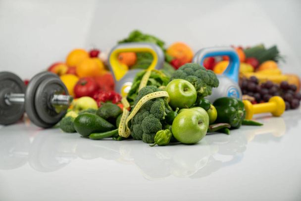Fitness koncepció. Egészséges táplálkozás: gyümölcsök és zöldségek. Felszerelés fitnesz feladatokhoz: mérőgép és súlyzók. Fehér háttér. - Fotó, kép