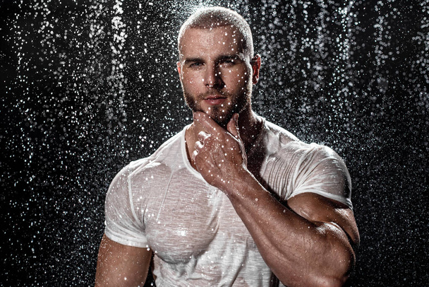 Muskularny mężczyzna pod deszczem w studio. sexy mężczyzna w woda krople - Zdjęcie, obraz