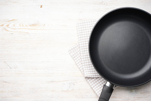 New frying pan and kitchen towel on a wooden background, space for text. Top view, flat lay. - Foto, imagen