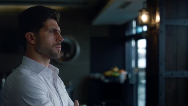 Charismatic businessman standing restaurant hall profile. Confident man resting lounge hotel bar. Elegant employee pondering business project in dark cafe. Scowling male face expression closeup. - Materiał filmowy, wideo