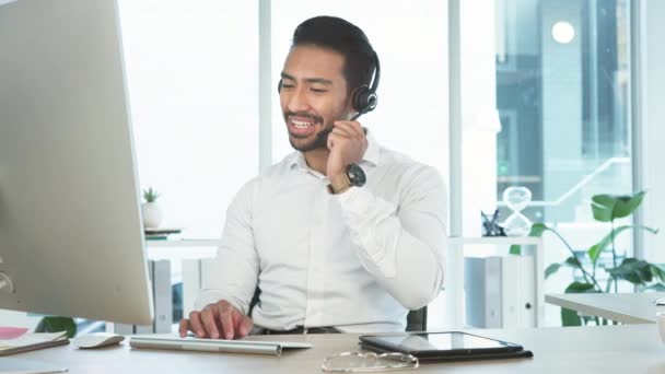Friendly call center agent using a headset while consulting for customer service and sales support on a computer in an office. Confident young business man operating a helpdesk and talking to clients. - Кадры, видео