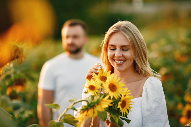 Young loving couple is kissing in a sunflower field. Portrait of couple posing in summer in field. - Foto, Imagen