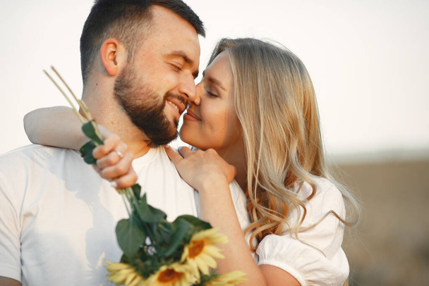 Young loving couple is kissing in a sunflower field. Portrait of couple posing in summer in field. - Foto, afbeelding