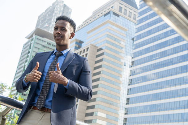 Business people thumbs up for acceptance. Portrait of an handsome businessman. Modern businessman. Confident young man in full suit standing outdoors looking away with cityscape - Фото, изображение