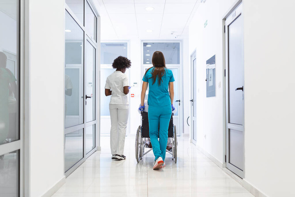 Wheelchair patient with professional African American female doctor and nurse specialist staff in corridor of hospital recovery center - Foto, Imagen