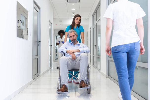 Wheelchair patient with professional female doctor and nurse specialist staff in corridor of hospital recovery center - Photo, Image