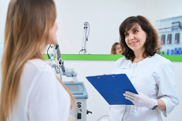 Smiling doctor looks at female client and fills out card - Foto, Bild