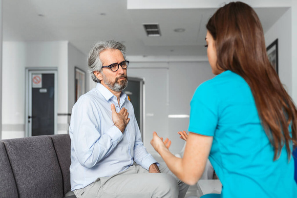 Patiënt met een arts in de wachtkamer die zijn symptomen bespreekt. Jonge vrouwelijke arts praten met haar patiënt en leg hem zijn opties en therapie - Foto, afbeelding
