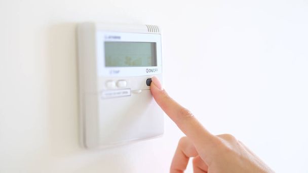 Climatizzatore digitale a parete e termostato domestico. Le dita femminili impostano comodi gradi di regolazione della temperatura nel soggiorno o nel primo piano dell'hotel - Foto, immagini