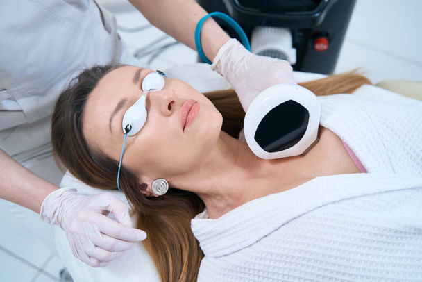 Woman in protective glasses lies on a skin rejuvenation procedure on phototherapy for neck skin rejuvenation neck - Фото, зображення