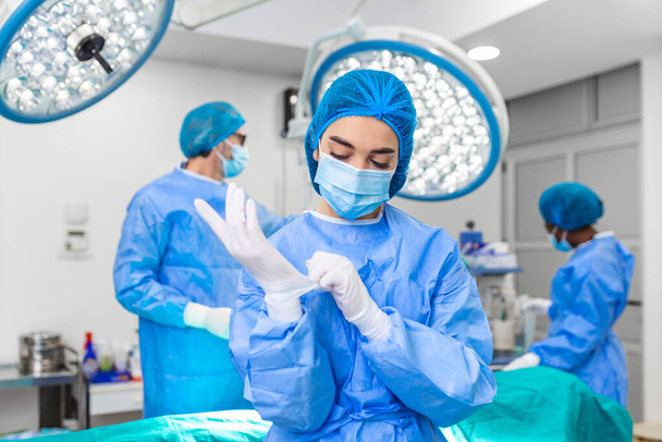 Portrait of female woman nurse surgeon OR staff member dressed in surgical scrubs gown mask and hair net in hospital operating room theater making eye contact smiling pleased happy looking at camera - 写真・画像