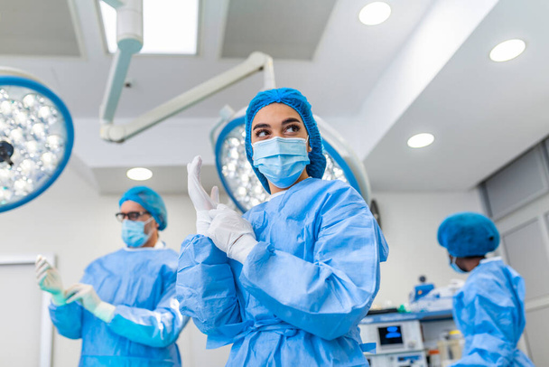 Portrait of female surgeon in surgical uniform in operation theater looking away. Doctor in scrubs and medical mask in modern hospital operating room. - Foto, Imagen