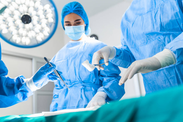 Group of surgeons doing surgery in hospital operating theater. Medical team doing critical operation. Group of surgeons in operating room with surgery equipment. Modern medical background - 写真・画像