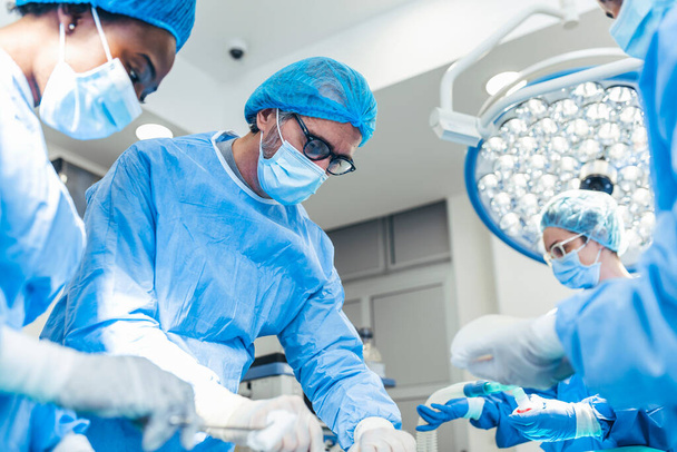 Surgery operation. Group of surgeons in operating room with surgery equipment. Medical background, selective focus. Surgeon team working together while operation - Photo, Image