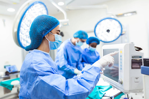 Anesthesiologist keeping track of vital functions of the body during cardiac surgery. Surgeon looking at camera. Doctor checking monitor for patient health status. - Photo, Image